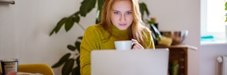 Kvinde sidder ved bord og kigger på bærbar pc