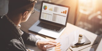 Mand Sidde Med Papir Foran Bærbar Pc Og Kikker På Grafer