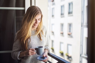 Smilende Kvinde Står Ved Åben Fransk Altan Med En Kop Kaffe