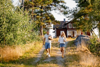 Mand Og Kvinde Går Med Bærbar Pc Under Armen Med Gammelt Træhus I Baggrunden