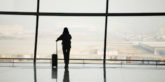 Kvinde silhuet med kuffert i lufthavn kigger ud af stort vindue