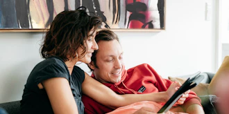 Kvinde Og Mand Sidder I Sofa Og Kikker På Ipad