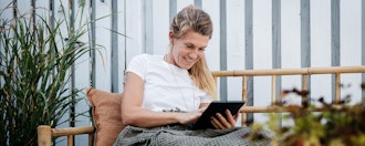 Kvinde Sidder I Havesofa Og Kikker På Ipad